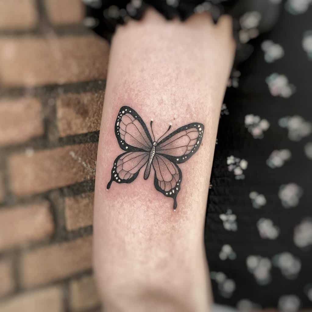 A black butterfly tattoo adorns a woman's arm,