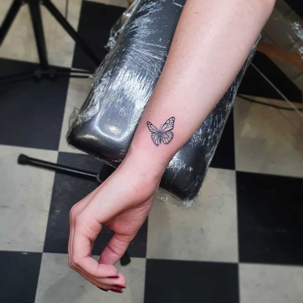 A delicate black butterfly tattoo graces a wrist