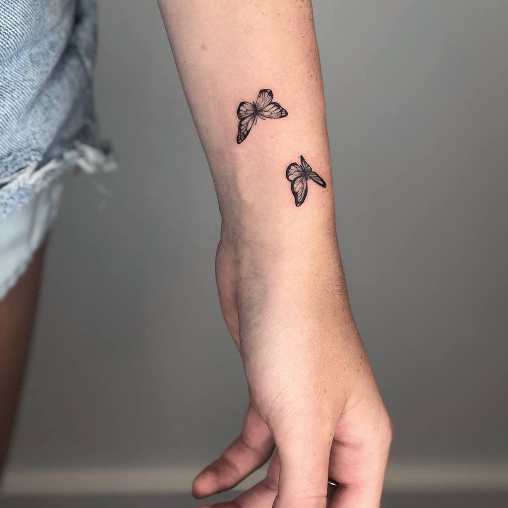 Wrist with two small black butterfly tattoos