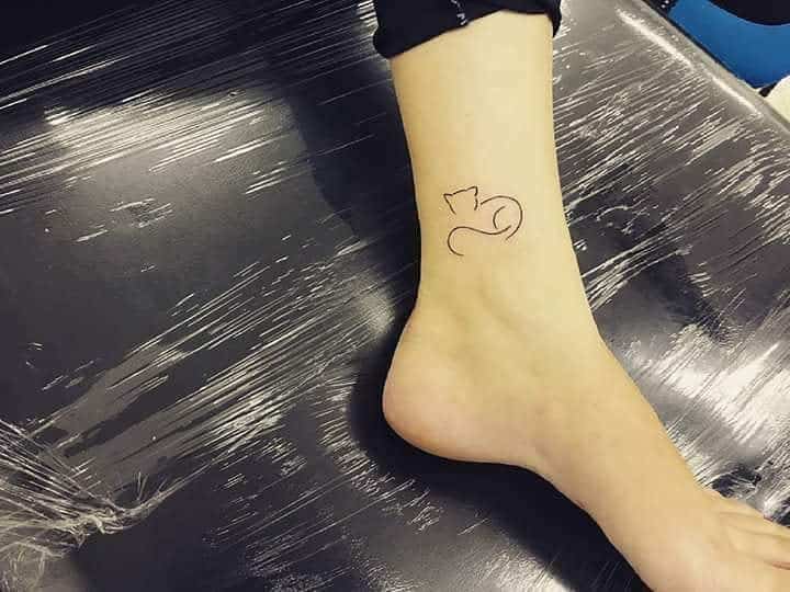 Tattoo of a minimalist cat outline adorning the side of a person's ankle, capturing elegant simplicity