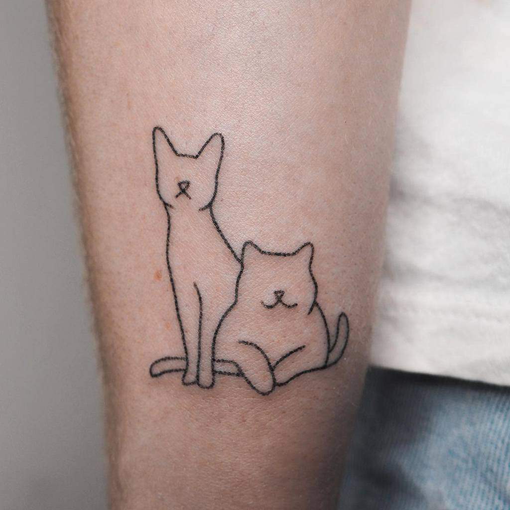 Tattoo of two minimalistic outlined cats, one standing and one sitting, gracefully inked on a person's arm