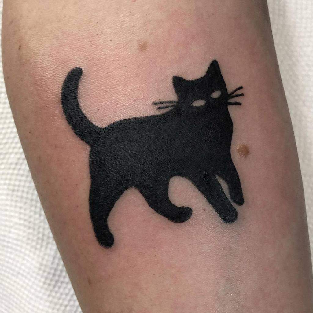 Black silhouette tattoo of a graceful cat with a lifted tail on a person's skin
