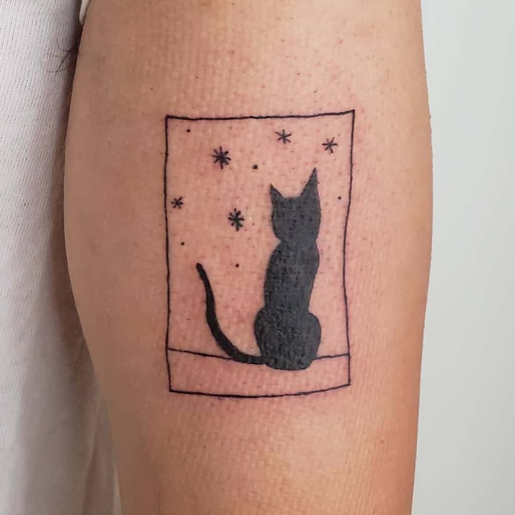 Tattoo of a black cat by a moonlit window, gazing at stars on a person's arm