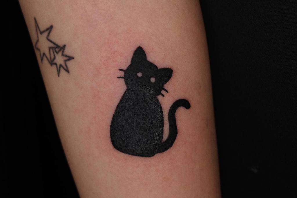 Tattoo of a sleek, black cat with a curly tail next to three small, outlined stars