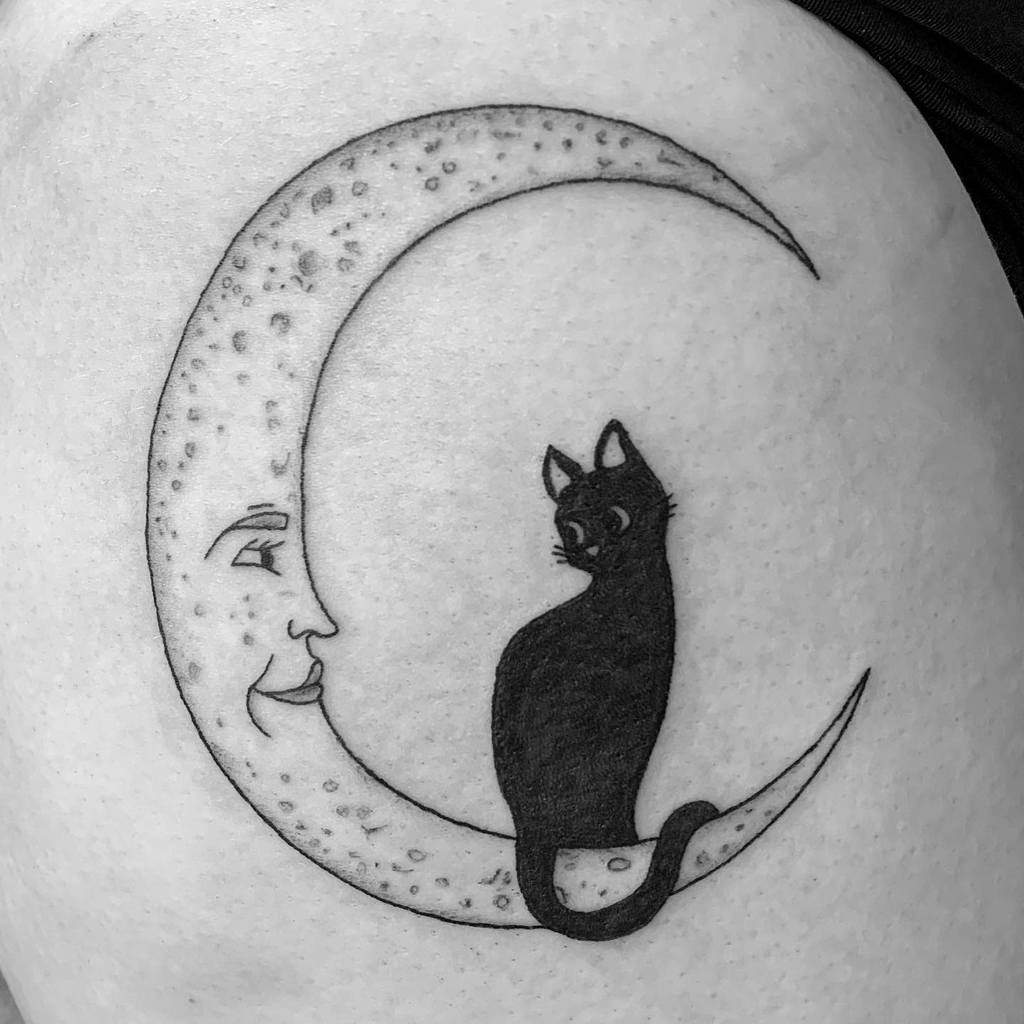 Tattoo of a crescent moon with a face, featuring a sleek black cat sitting inside the curve