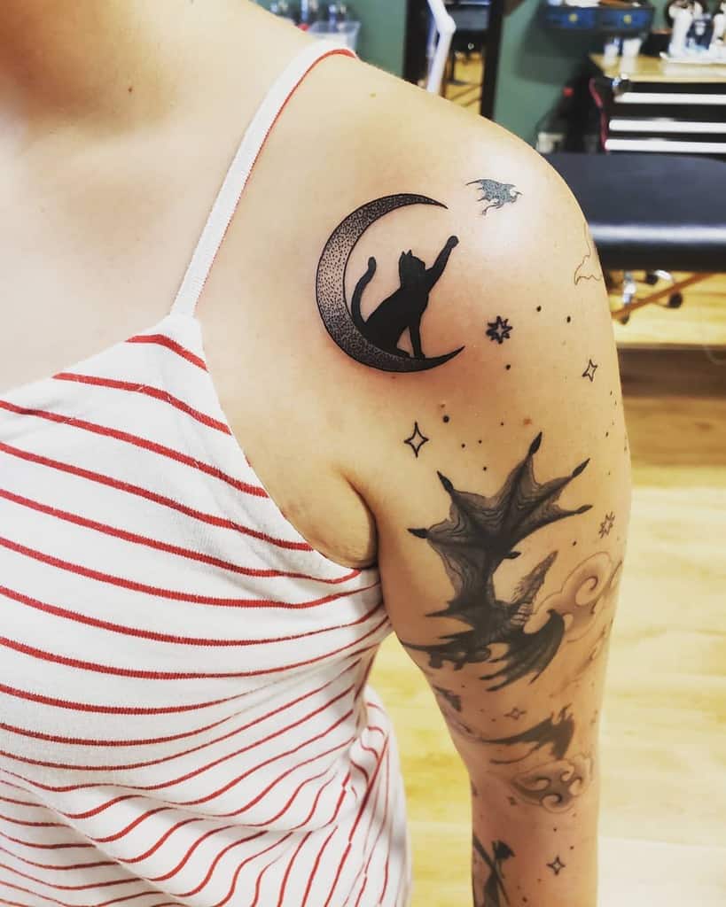 Person with a tattoo of a cat on a crescent moon on the shoulder