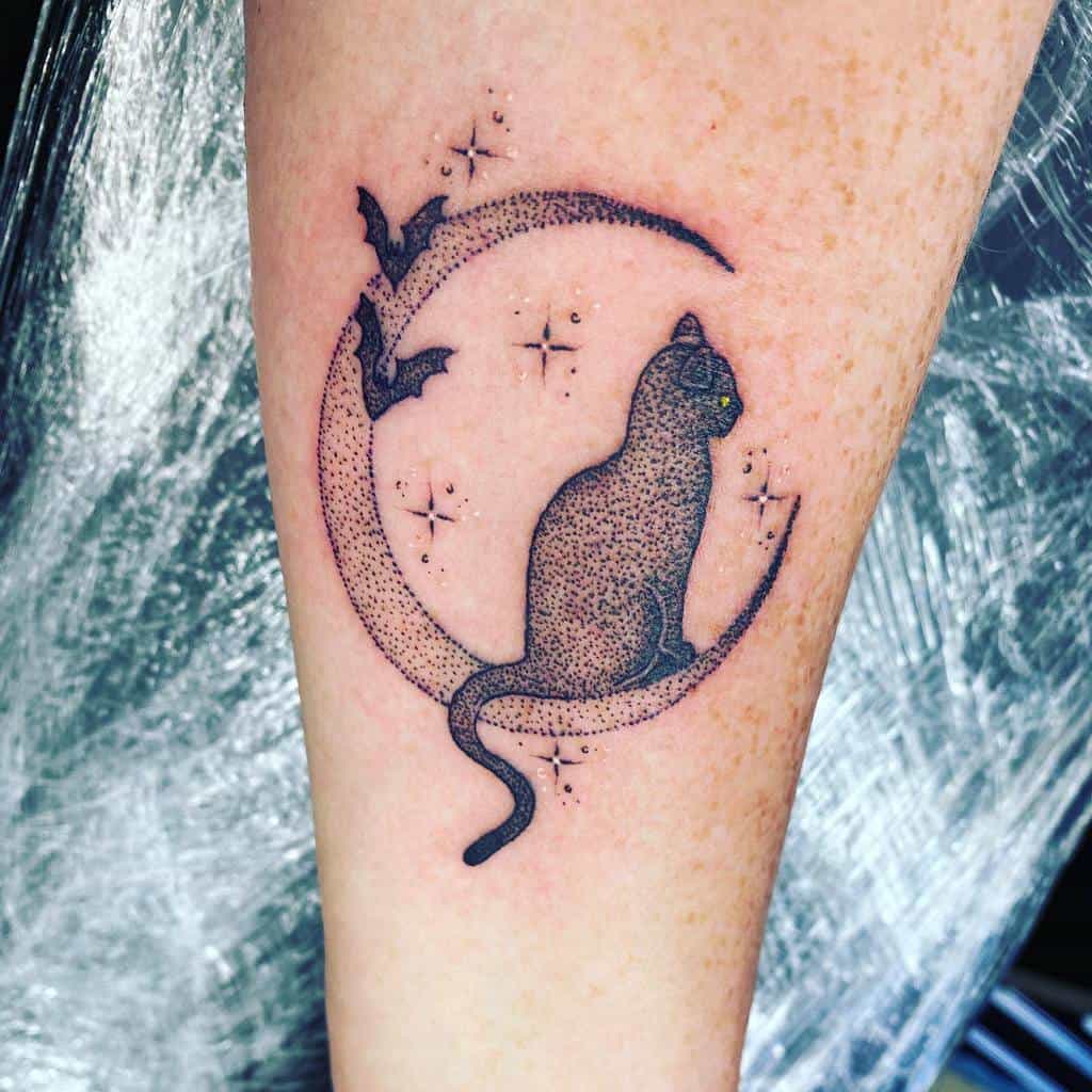 A mesmerizing tattoo of a cat perched on a crescent moon, surrounded by bats and stars, graces the person's arm
