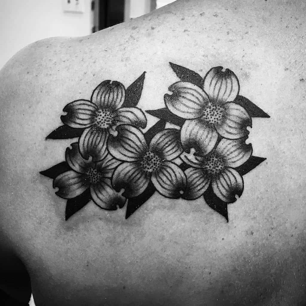 A black and white tattoo of two clusters of dogwood flowers graces a shoulder