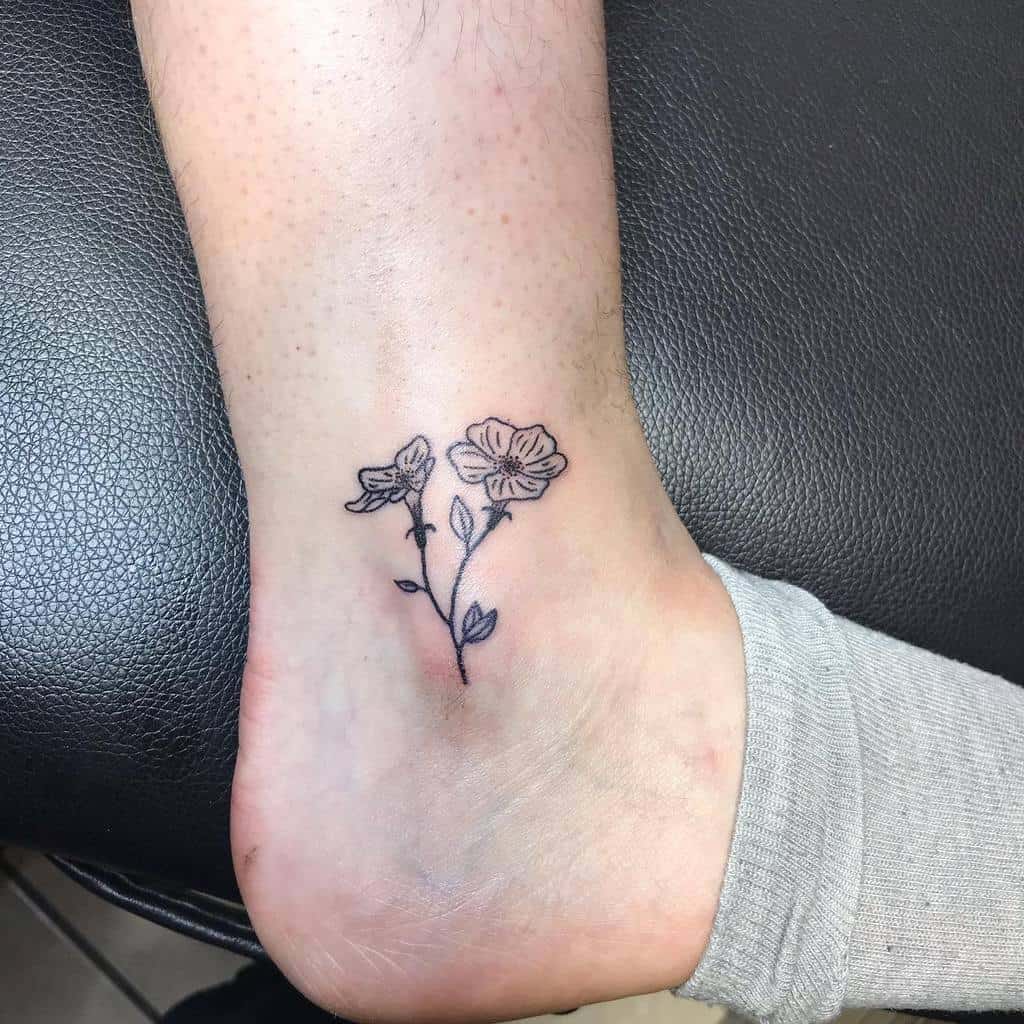 Tattoo of two simple dogwood flowers on a person's ankle