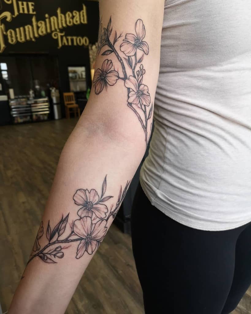 A floral tattoo graces a person's arm, showcasing delicate branches and dogwood flowers meticulously rendered in black ink