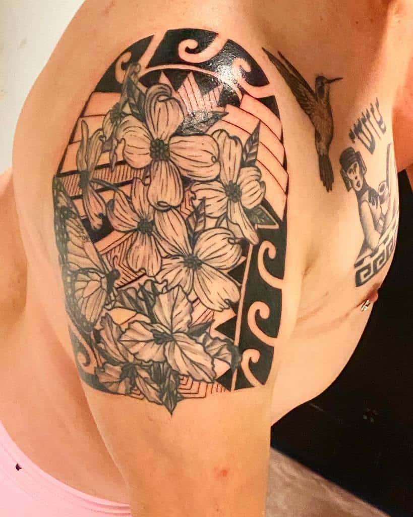 Tattoo of dogwood flowers intertwined with geometric patterns and a bird design on an upper arm