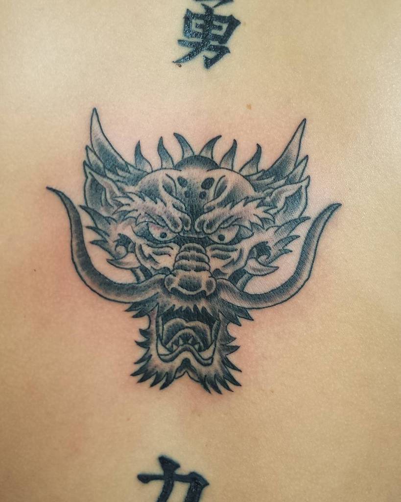 Tattoo showcasing a majestic dragon head, framed by intricate Chinese characters elegantly placed above and below it