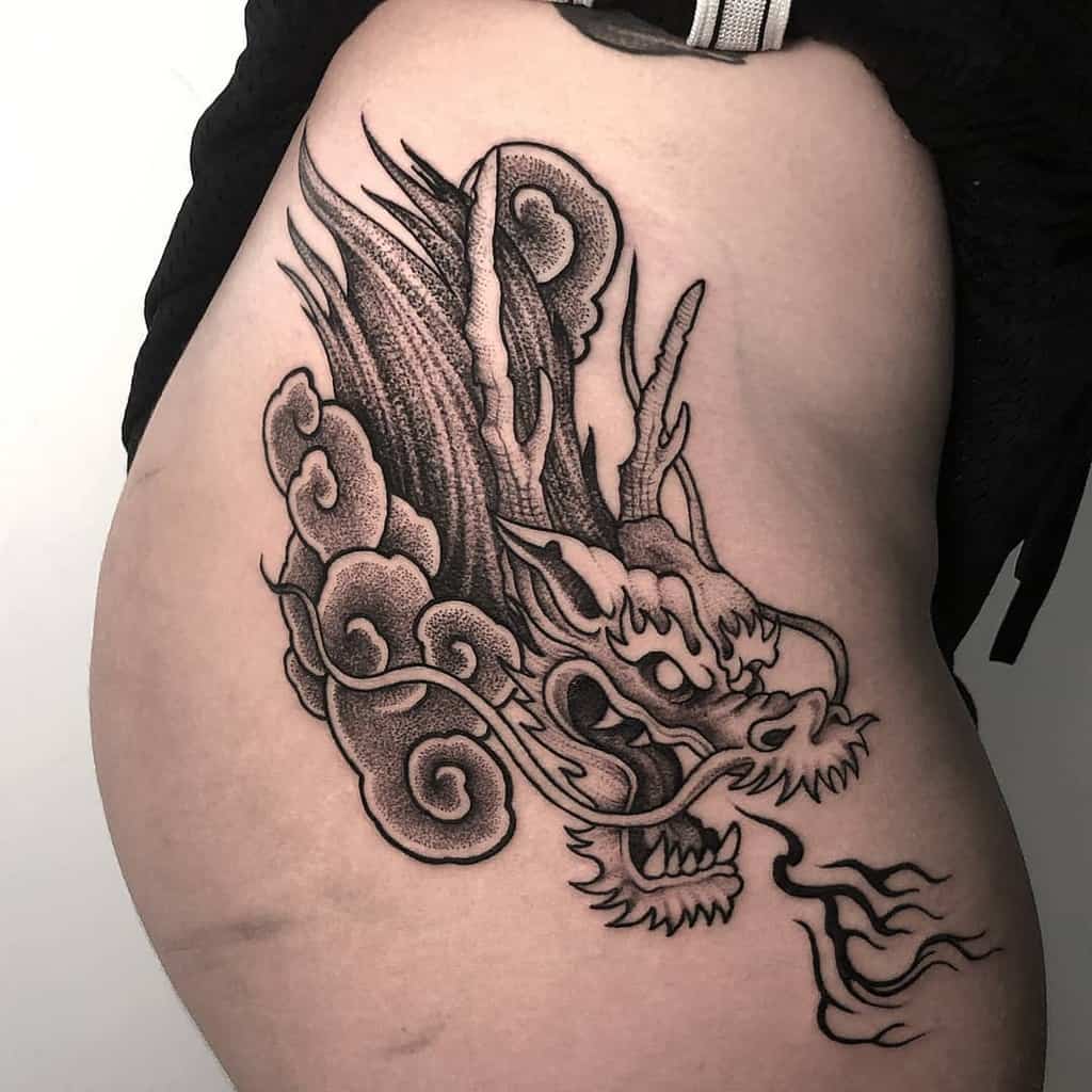 Black dragon head tattoo with flames and clouds elegantly etched on a person's side