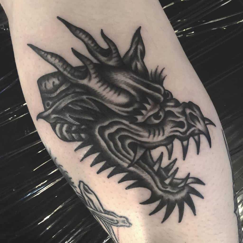 Black and gray dragon head tattoo on skin with sharp spikes and fierce expression