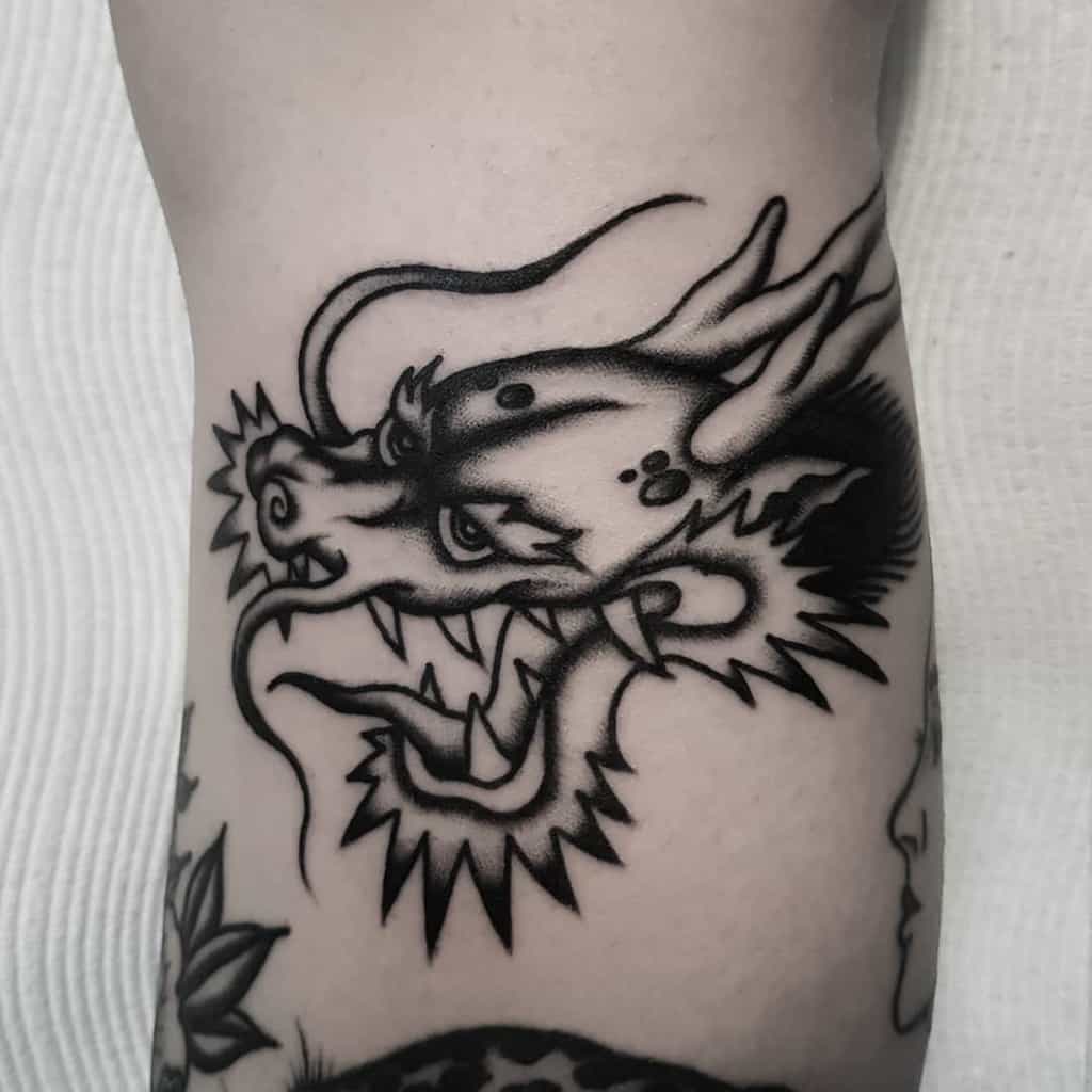 Black dragon head tattoo with bold lines and stylized features on skin
