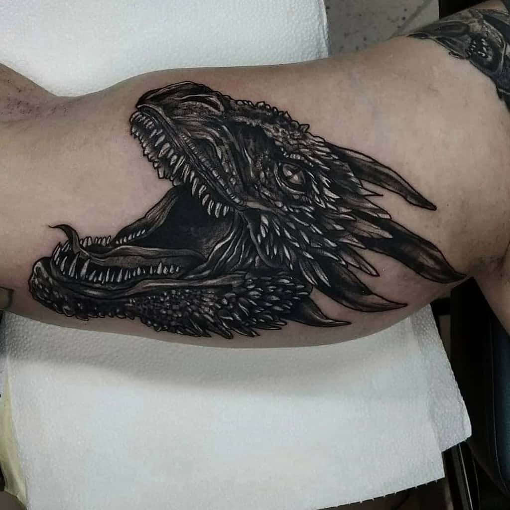 Tattoo of a roaring dragon head, with intricate detailing, on a person's upper arm