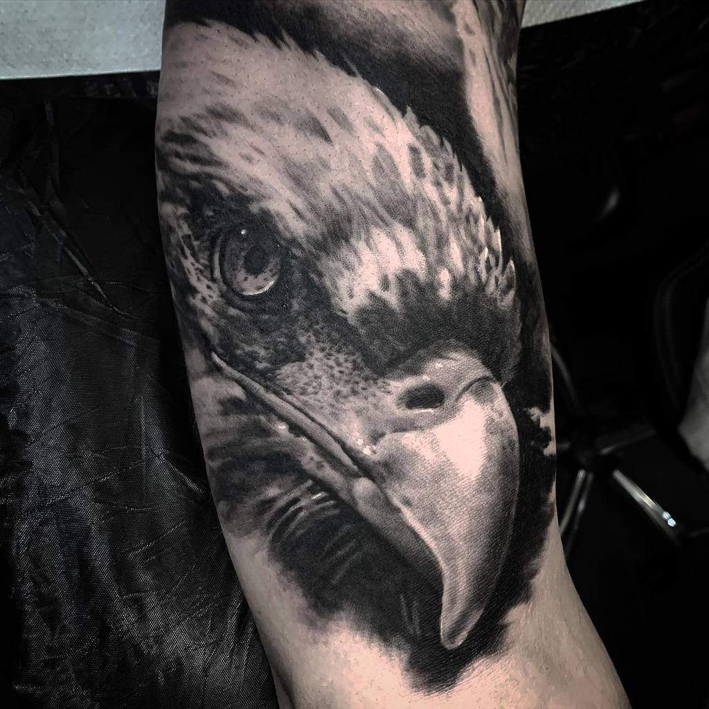 Tattoo of a detailed eagle head on an arm highlighting the eagle's sharp eye and beak in grayscale