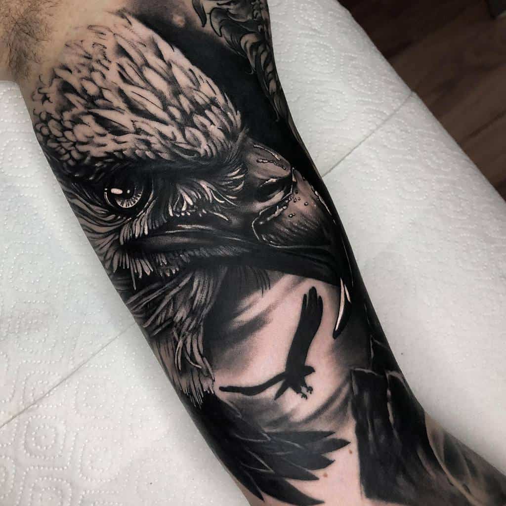 Black and grey tattoo of a detailed eagle head with a flying bird in the background on a forearm