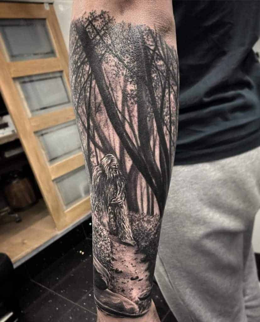 Forearm tattoo depicting a forest scene with a figure resembling Bigfoot
