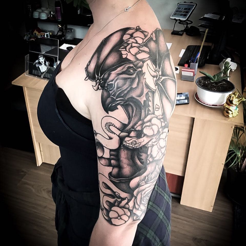 Striking black-and-grey half-sleeve tattoo featuring a fierce bird of prey, floral elements, and intricate details