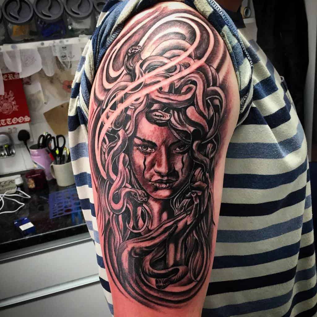 Half sleeve tattoo of a Medusa face with snake hair on a woman's upper arm