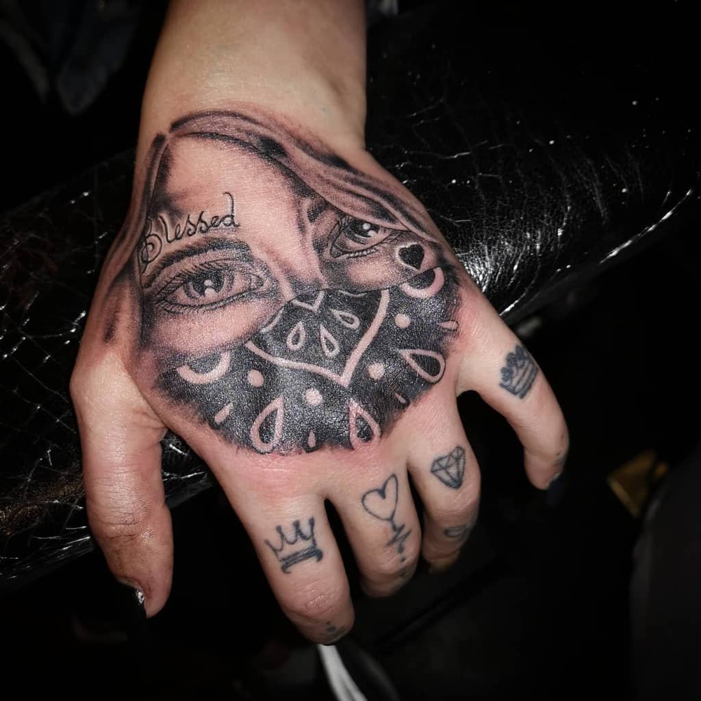 Realistic black and grey tattoo of a veiled woman with expressive eyes, a decorative bandana, and "Blessed" scripted above