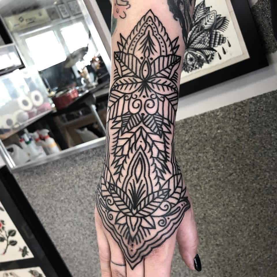 Bold black geometric and mandala-style tattoo featuring intricate symmetrical patterns and linework.