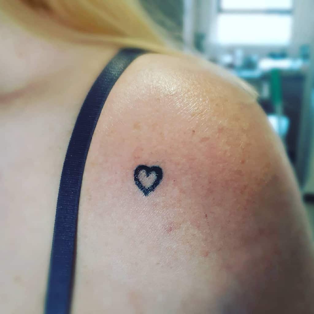Small black heart tattoo on a woman's shoulder