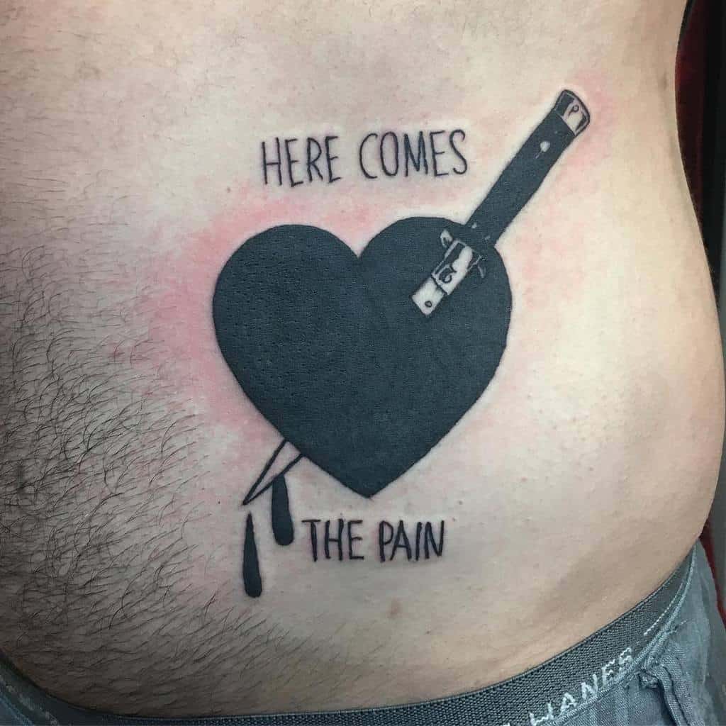 Black heart tattoo with a knife piercing through it, dripping ink, and the phrase 'Here Comes the Pain
