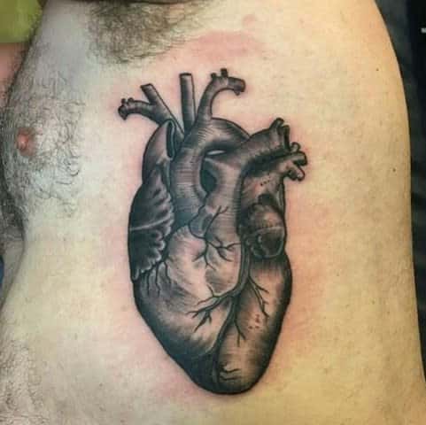 Realistic black tattoo of a human heart with detailed shading and anatomical features, emphasizing the organ's complexity
