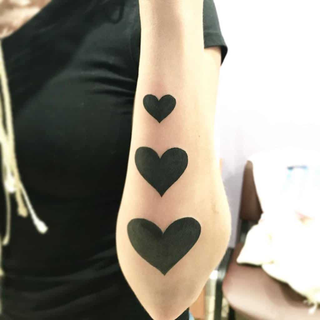 Three solid black heart tattoos of descending size aligned vertically