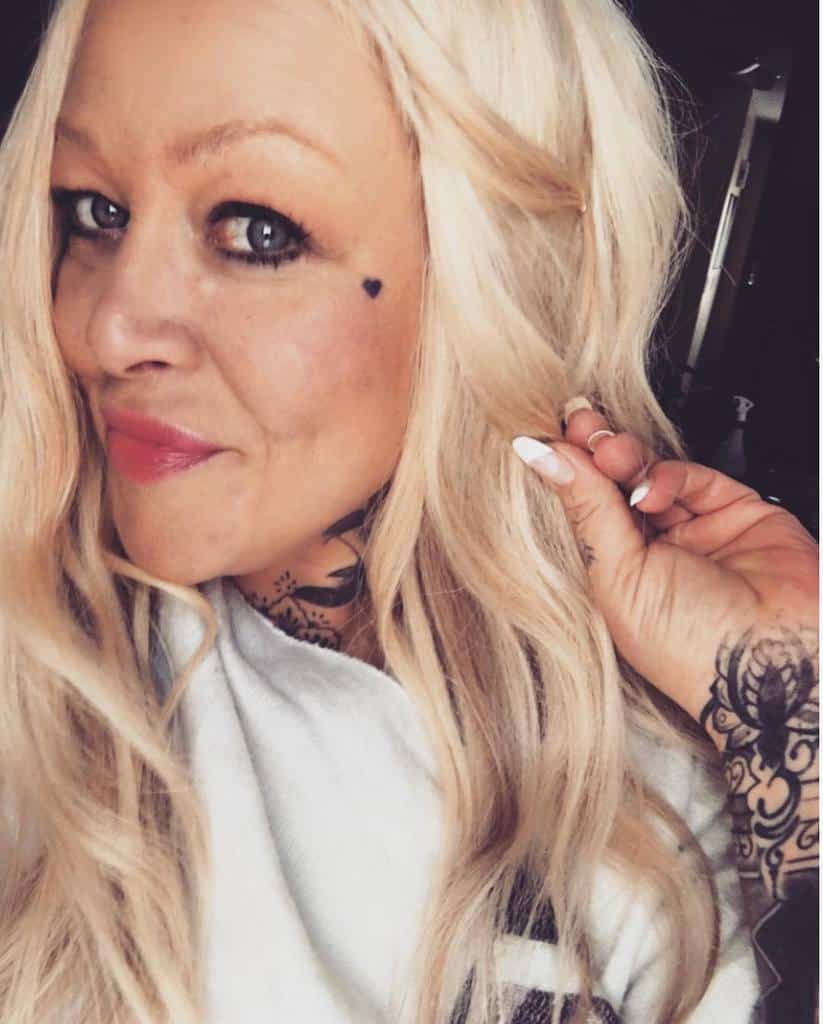 A small black heart tattoo under her eye, along with intricate tattoos on her neck and hand