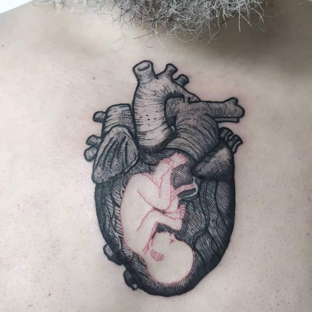 Realistic black tattoo of a human heart with a detailed fetus inside, showcasing intricate shading and anatomical precision