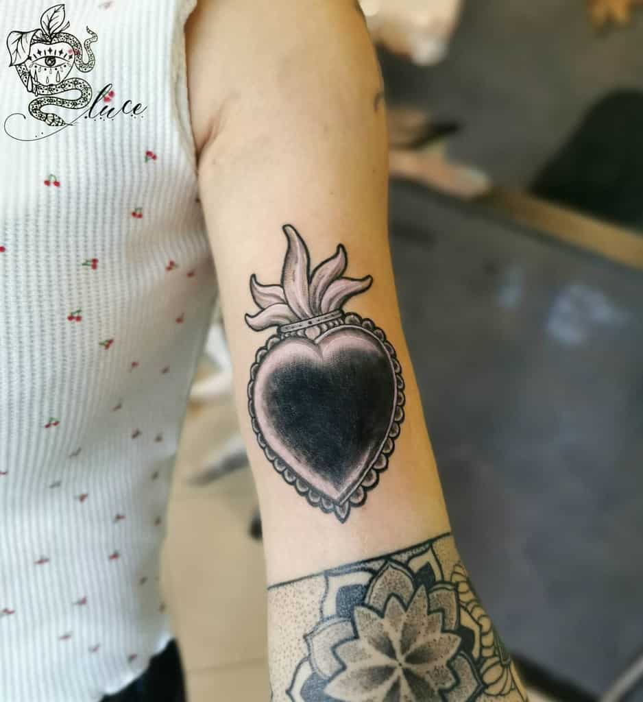 Elegant tattoo featuring a black heart encased in a lace-like border and crowned with a decorative baroque flourish