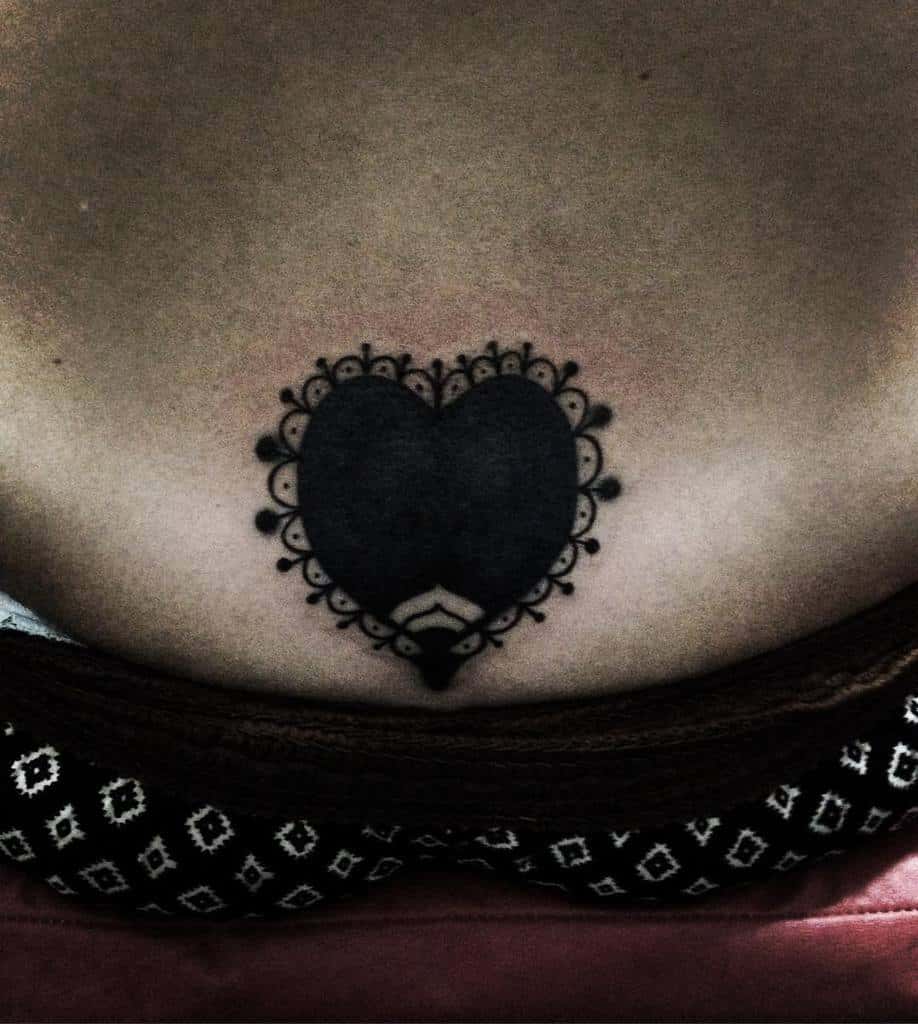 Black heart tattoo framed by a delicate lace-like border, creating a bold yet intricate design