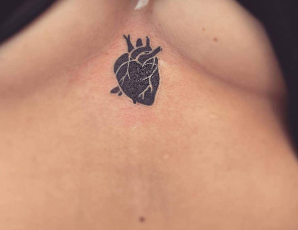 Close-up of a small, detailed anatomical black heart tattoo, artistically rendered in black ink