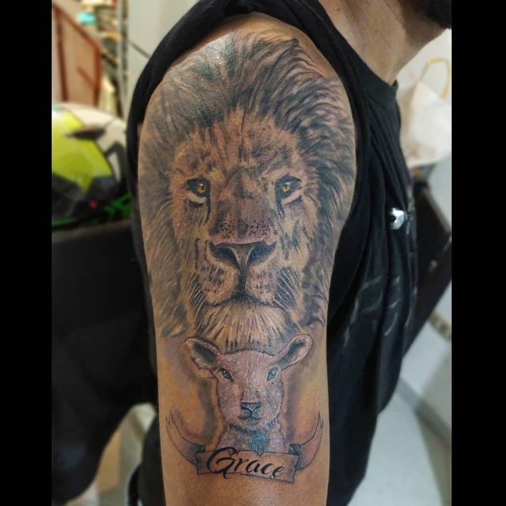 A stunning tattoo featuring a lion and lamb intertwined with the elegant word "Grace" adorns the person's upper arm