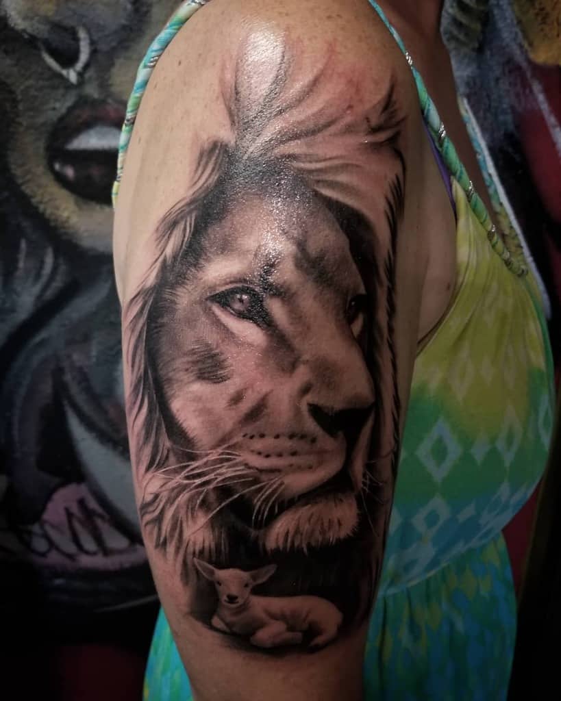 A realistic lion tattoo on a person's upper arm, featuring a lion and a lamb in intricate detail