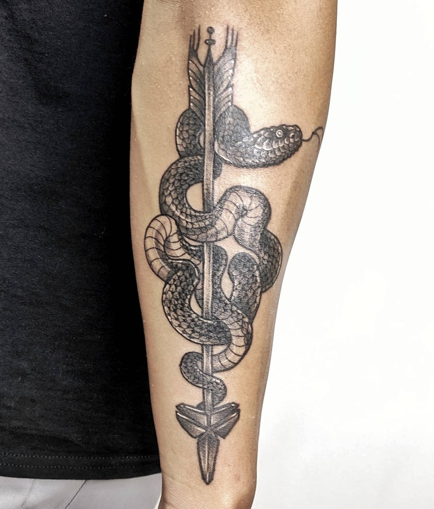 Arm tattoo featuring a black mamba coiled around an arrow