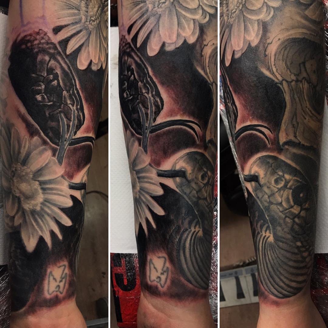 Tattooed arm sleeve with a serpent, flowers, and a small butterfly on the forearm