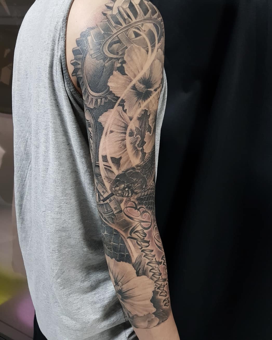 Sleeve tattoo of mechanical gears, flowers, and a snake on an arm