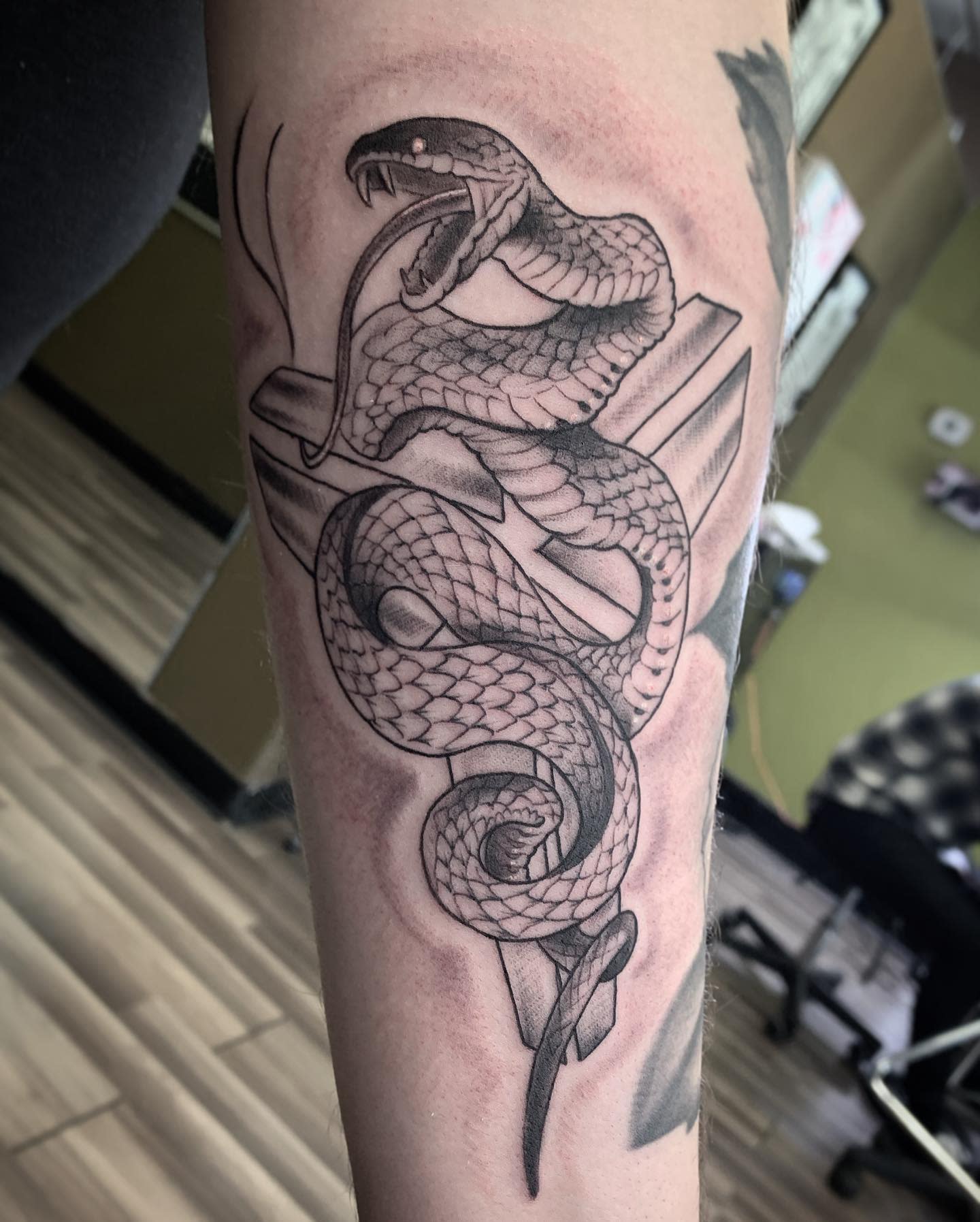 Black and white tattoo of a black mamba coiled around a sword on a forearm