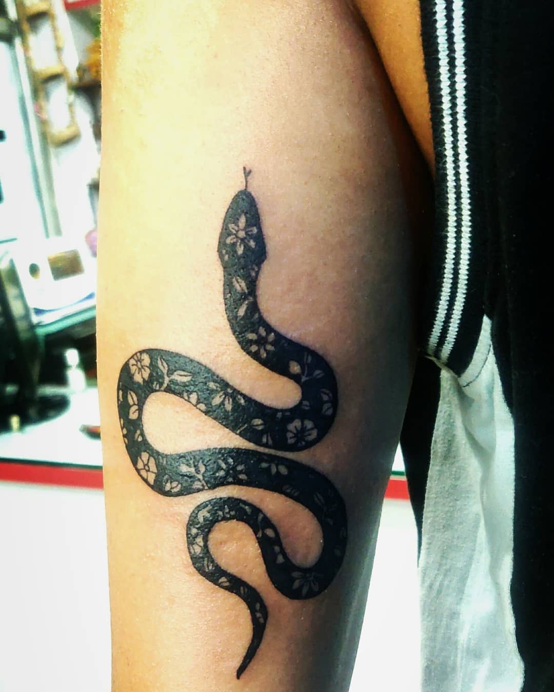 Black snake tattoo with floral pattern on upper arm