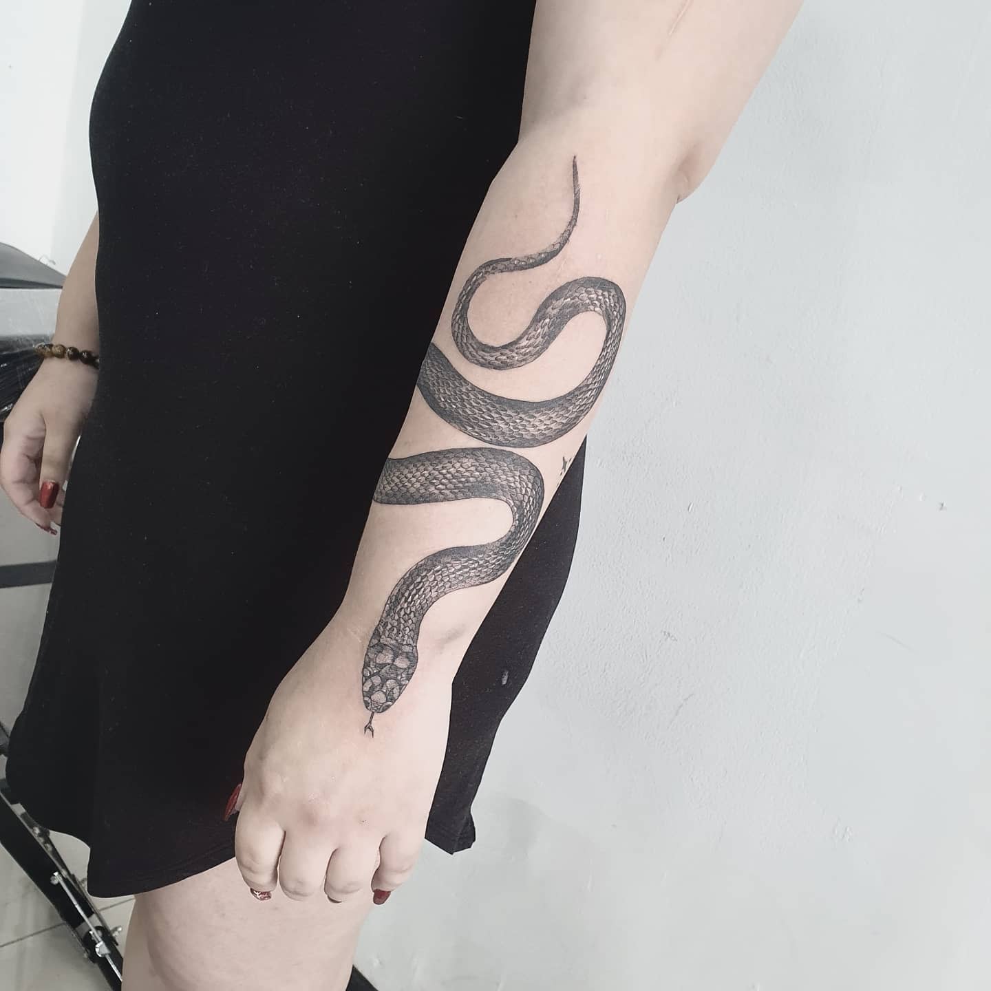 Black dress wearer displays a black mamba tattoo on forearm