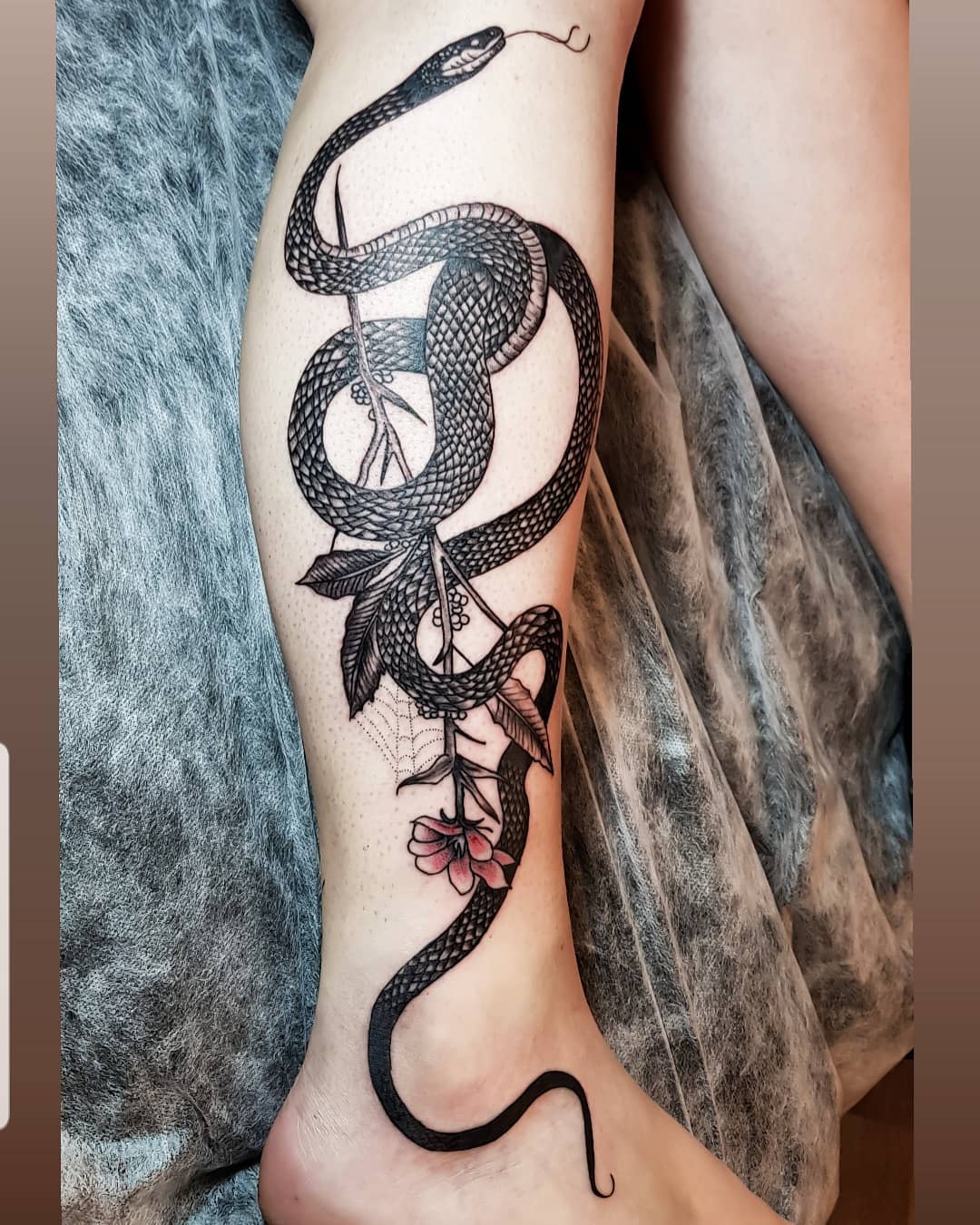 Tattoo of a black mamba snake wrapped around flowers and leaves on a leg