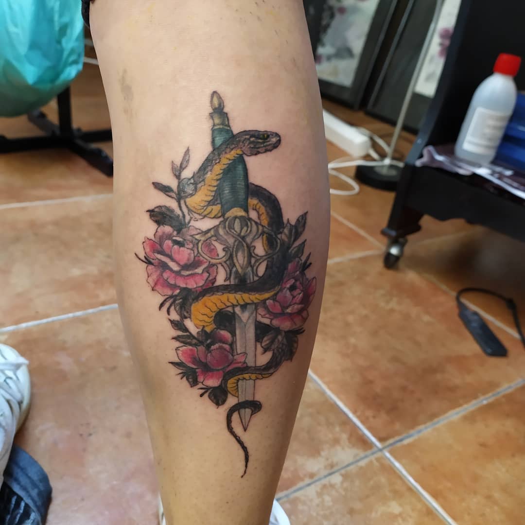 Tattoo featuring a serpent coiled around a sword, surrounded by pink flowers on a leg