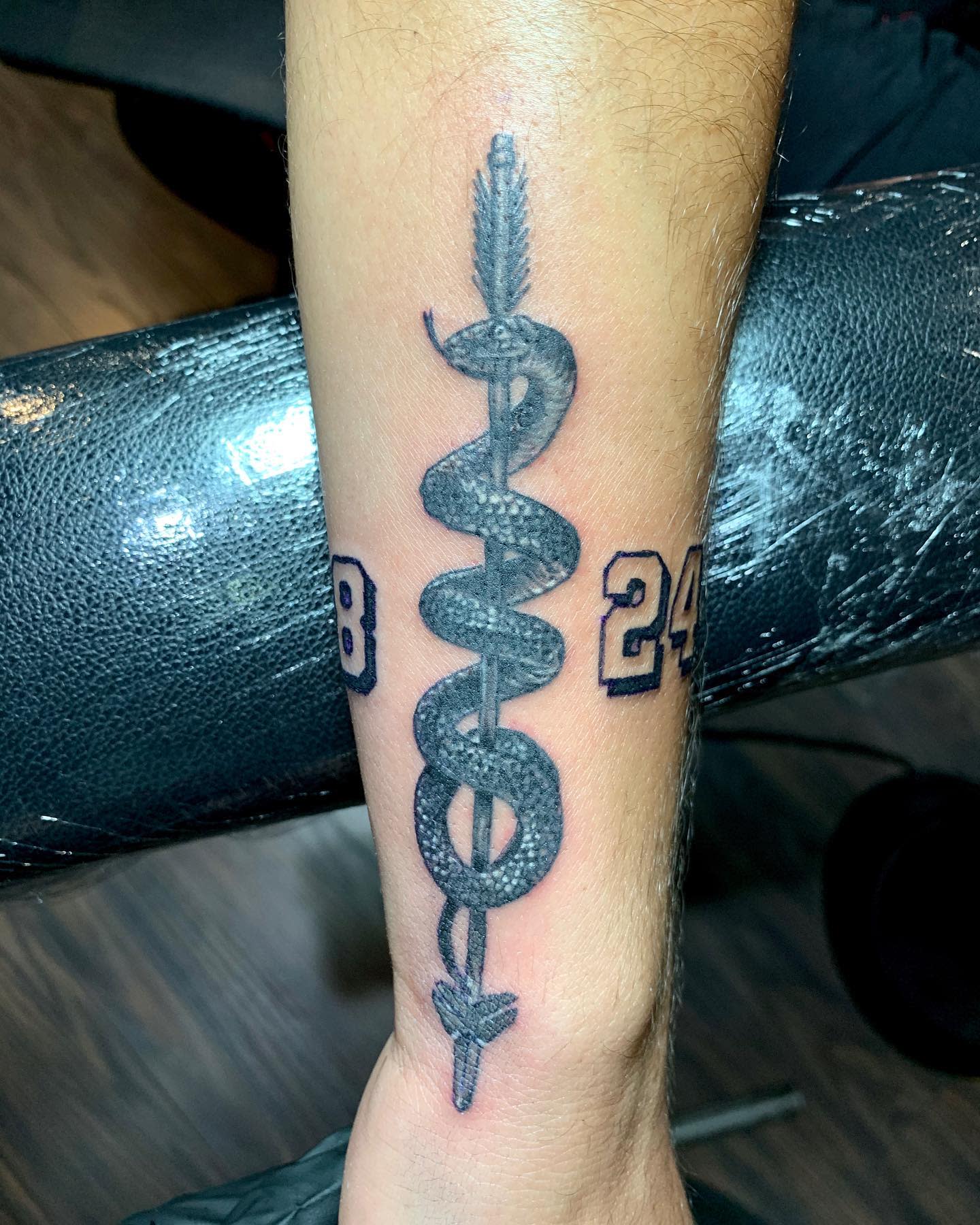 Tattoo of a caduceus with numbers 8 and 24 on an arm