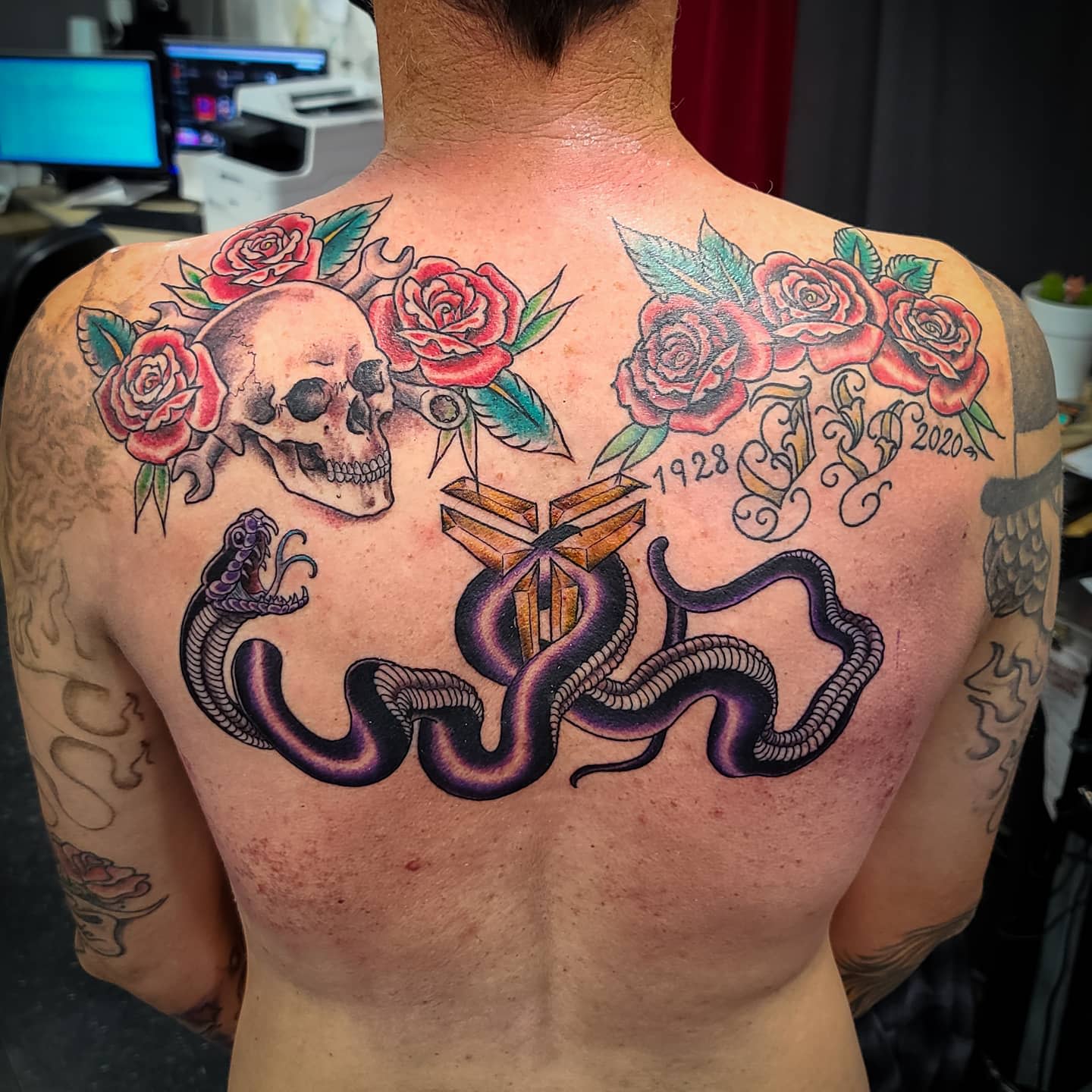Tattooed back featuring a skull, roses, and two black snakes entwined around a cross and numbers