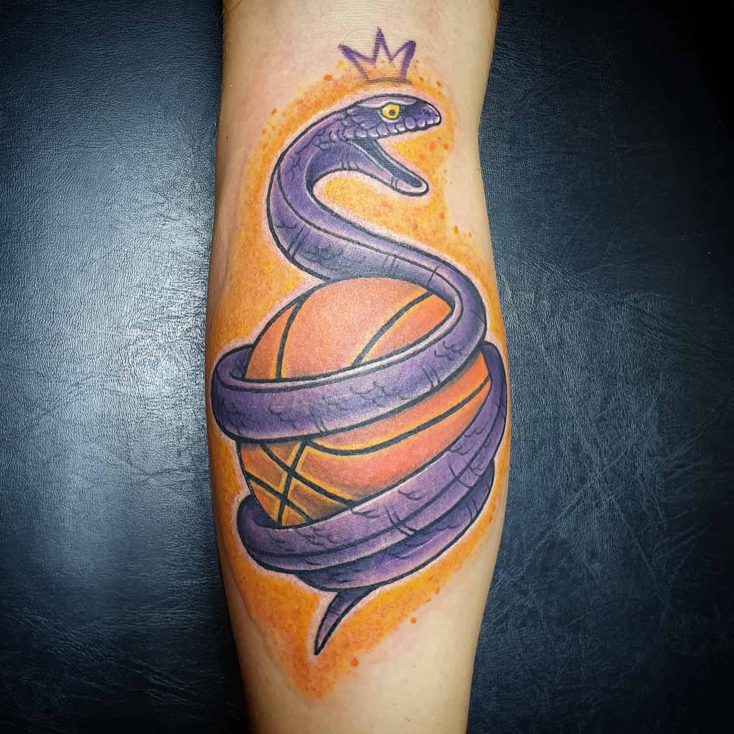 Tattoo of a purple black mamba coiled around a basketball with a crown on the snake's head
