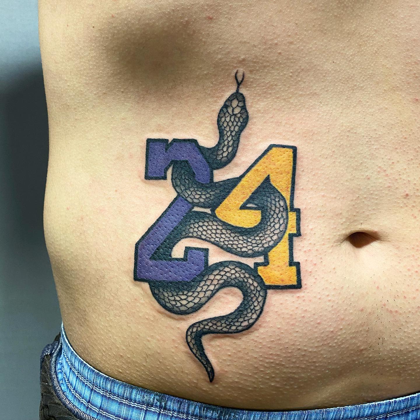 Tattoo of a black mamba intertwined with the numbers 24 on someone's ribcage